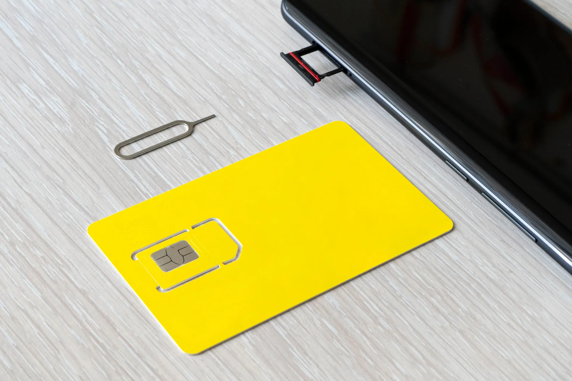 Carte SIM jaune avec sa puce prédécoupée, outil d'éjection et smartphone dont le tiroir SIM est ouvert, posés sur un bureau clair