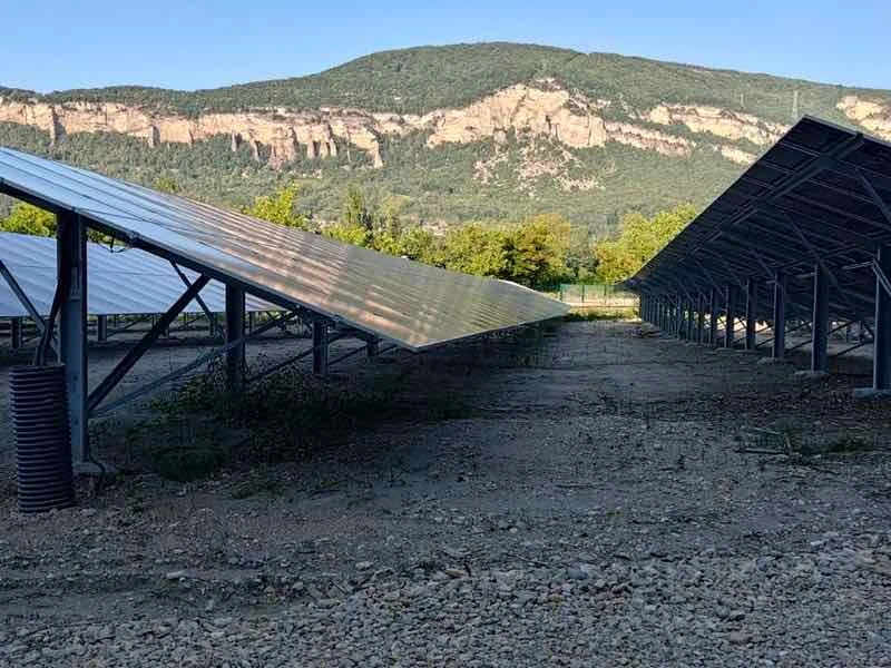 Rangées de panneaux solaires au sol sur un terrain caillouteux, avec des falaises calcaires en arrière-plan