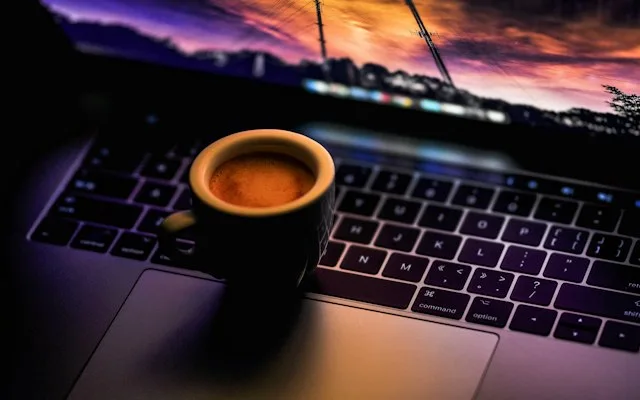 Tasse de café posée sur un ordinateur portable au crépuscule