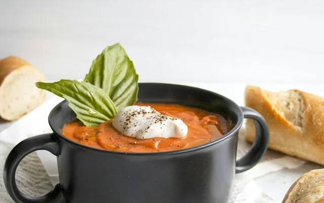 Mug noir rempli de soupe de tomate, une feuille de basilic dessus
