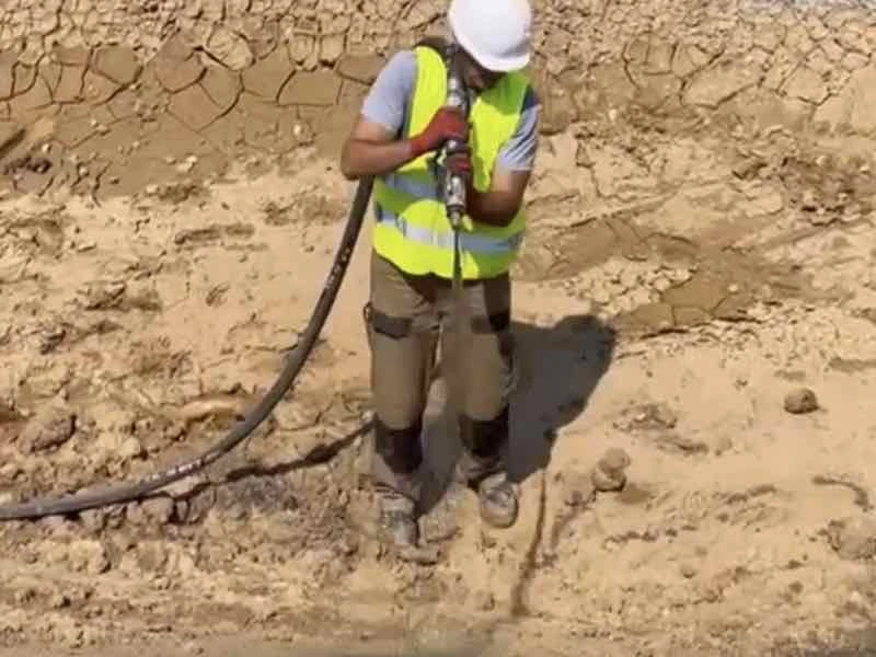 Ouvrier casqué en gilet jaune projetant le mélange au fond d'un bassin de terre sèche et craquelée