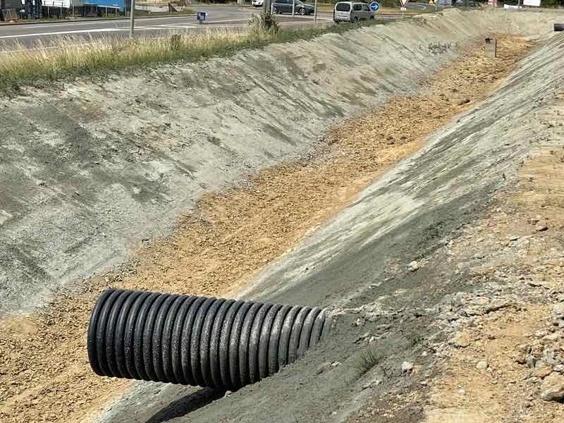 Talus d'un bassin de rétention en bord de route recouvert du mélange projeté, avec une buse de drainage noire au premier plan