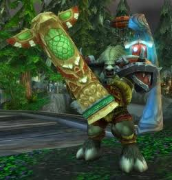 Un Tauren chaman en armure verte brandit une immense masse à deux mains sculptée en forme de totem, vert et or, dans une forêt