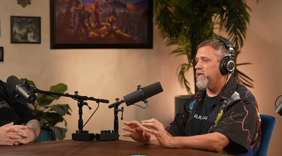 Un développeur grisonnant au casque, en chemise noire à motifs violets, parle les mains ouvertes devant un micro dans le studio du podcast